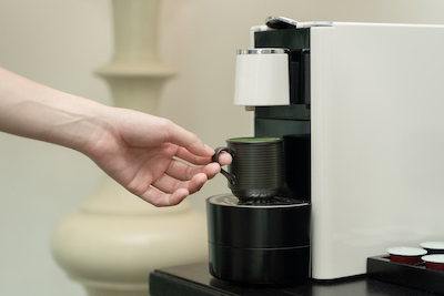 Coffee capsule machine maker. Hand takes a ceramic cup of coffee on the coffee machine.
